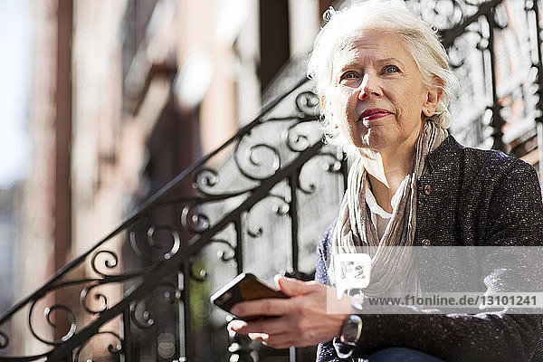 Nachdenkliche ältere Frau hält Smartphone im Freien