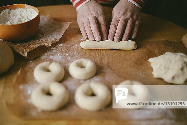 Abgehackte Hände einer Frau  die zu Hause in der Küche auf einem Holztisch Donuts zubereitet