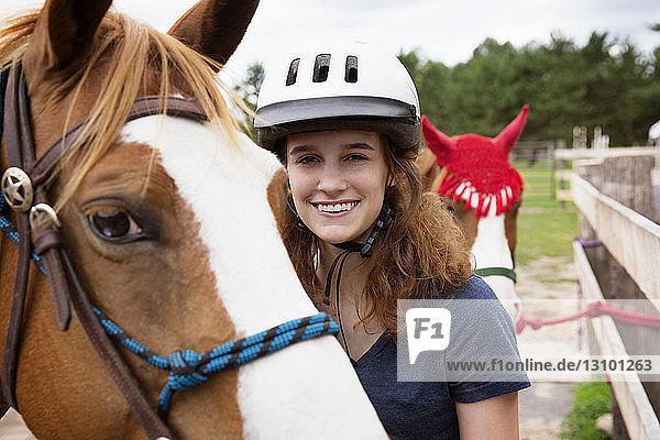 Portrait of happy teenage girl standing with horses on field