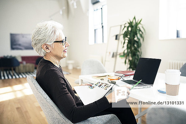 Senior businesswoman holding document and sitting on chair in office