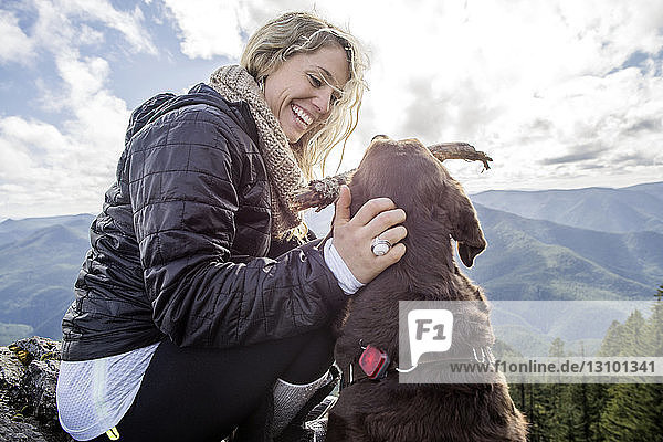 Niedrigwinkelansicht einer glücklichen Frau  die mit einem Hund auf einem Bergfelsen spielt