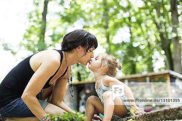 Liebende Tochter küsst Mutter auf den Mund  während sie im Hinterhof sitzt