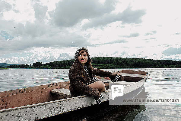Girl looking away while sitting in rowboat on lake against cloudy sky