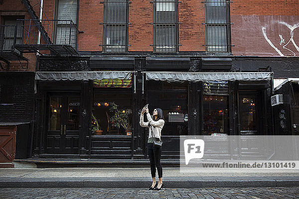 Frau fotografiert durch Mobiltelefon  während sie vor dem Gebäude steht