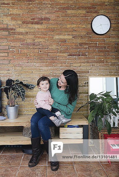 Glückliche Mutter mit Tochter sitzt zu Hause auf einem Holztisch