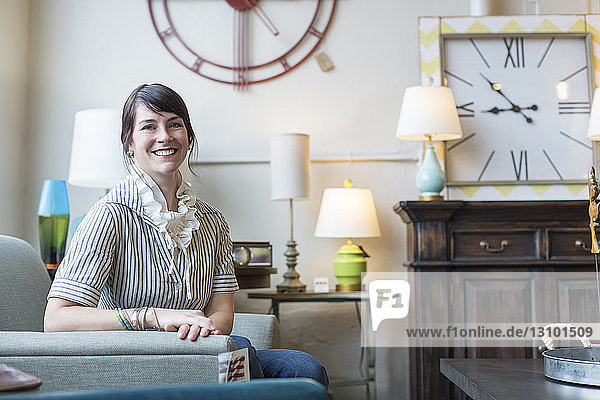 Portrait of smiling owner sitting on armchair in furniture store