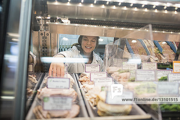 Female worker arranging food in display cabinet at supermarket