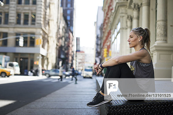 Nachdenklicher Sportler entspannt sich auf dem Bürgersteig in der Stadt