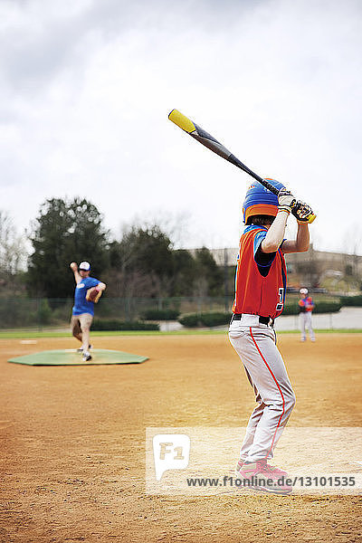 Seitenansicht eines Baseball spielenden Jungen mit Trainer auf dem Feld gegen den Himmel