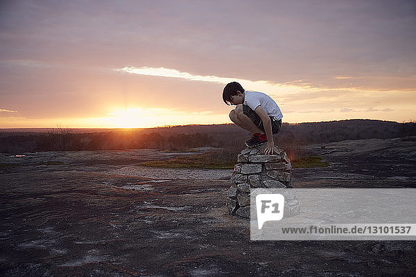 Junge sitzt auf Felsen am Berg Arabia vor bewölktem Himmel bei Sonnenuntergang