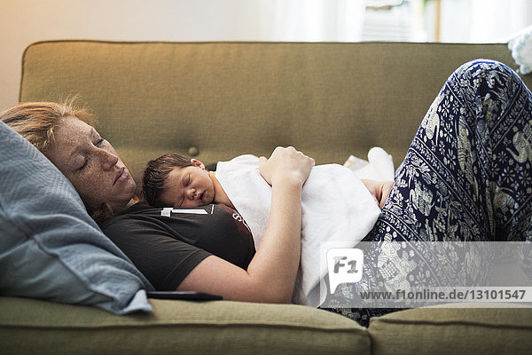 Side view of woman sleeping with baby boy on sofa at home