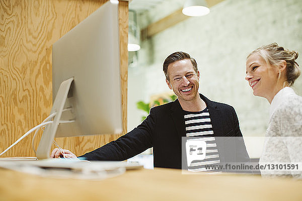 Lächelnde Geschäftsleute  die im Büro auf den Desktop-Computer schauen
