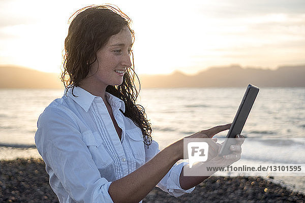 Frau benutzt Tablet-Computer  während sie am Ufer gegen den Himmel steht