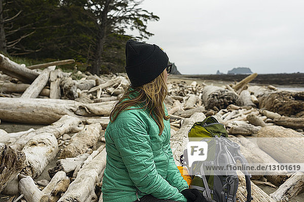 Nachdenkliche Wanderin schaut weg  während sie an der Olympic Coast auf Baumstämmen sitzt