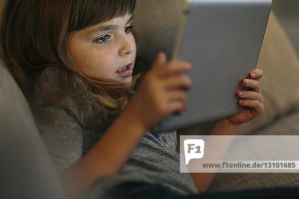 Hochwinkelaufnahme eines Mädchens  das einen Tablet-Computer benutzt  während es zu Hause auf dem Sofa liegt