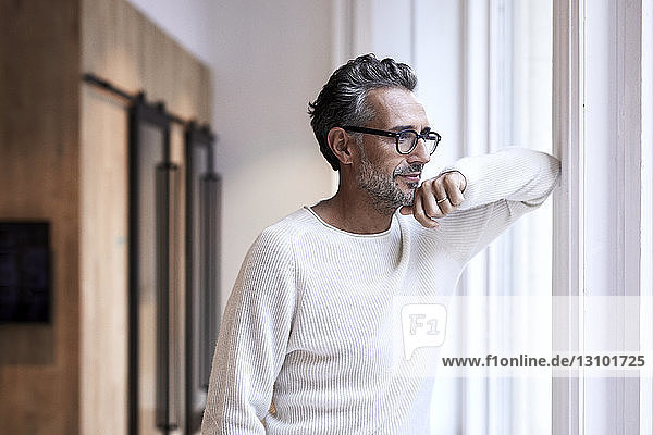 Thoughtful mature businessman standing by window at creative office
