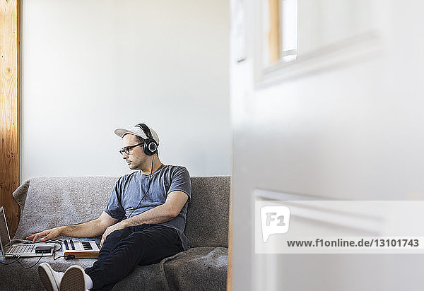 Man listening music while using laptop computer on sofa seen through doorway