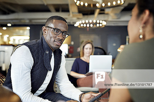 Geschäftsleute  die sich mit einer Kollegin am Laptop im Hintergrund im Kreativbüro unterhalten