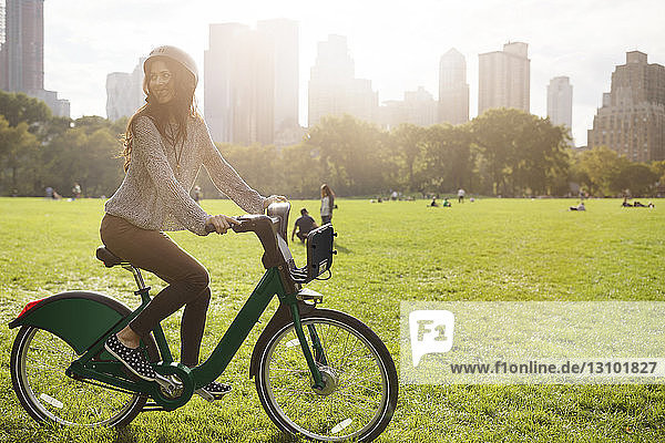 Woman looking away while riding bicycle on grassy field