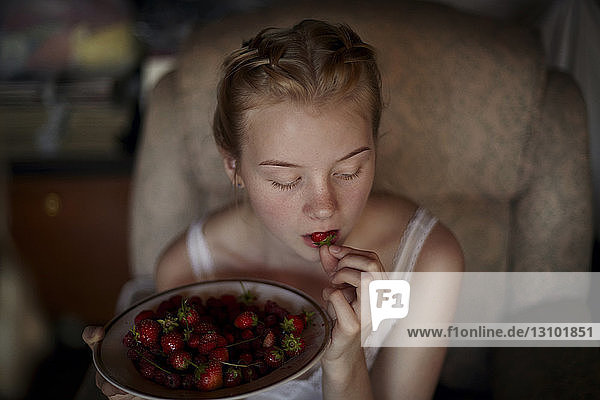 Hochwinkelaufnahme einer Frau  die zu Hause sitzend Erdbeeren isst