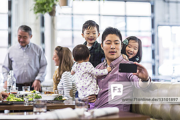 Vater nimmt Selfie mit Kindern  während er mit der Familie im Restaurant sitzt