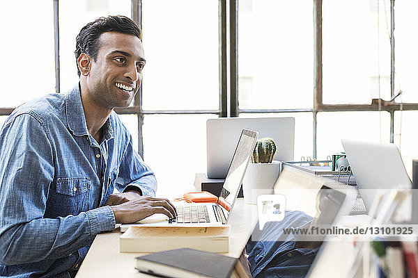 Lächelnder Geschäftsmann mit Laptop am Schreibtisch im Büro