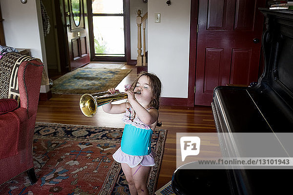Schrägaufnahme eines Mädchens  das Trompete spielt  während es zu Hause am Klavier steht
