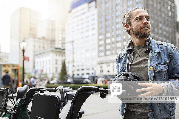 Smiling man looking away while standing by bicycle at parking lot