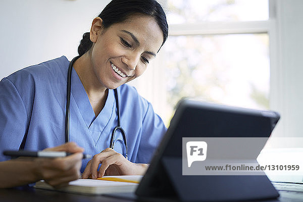 Lächelnde Ärztin schreibt während der Arbeit am Schreibtisch im Krankenhaus Tagebuch