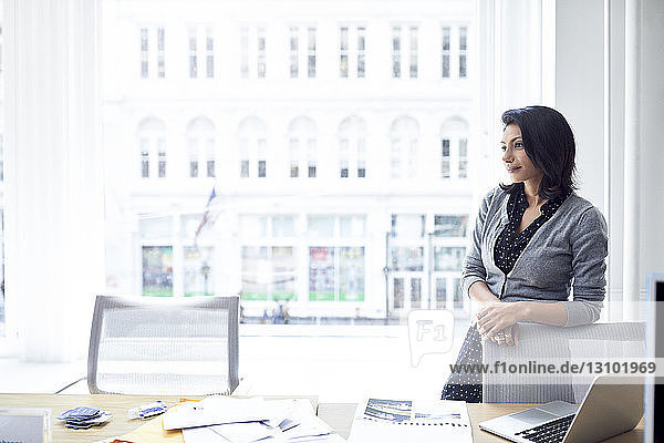 Nachdenkliche Geschäftsfrau schaut weg  während sie im Amt an einem Fenster steht