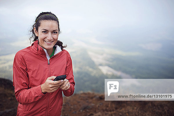 Portrait of woman text messaging while standing on mountain