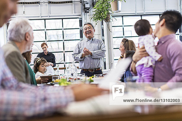 Family looking at senior man talking while standing at table in restaurant