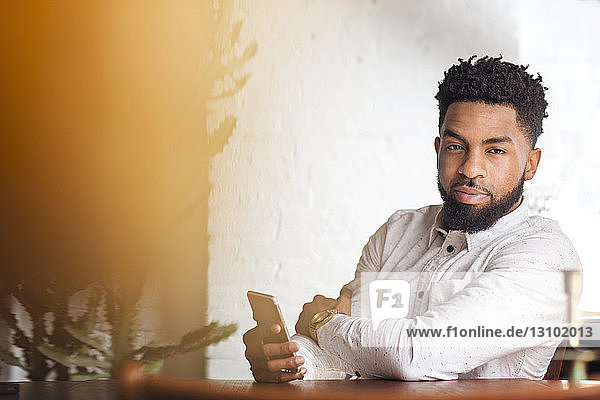 Portrait of confident man holding smart phone sitting at table