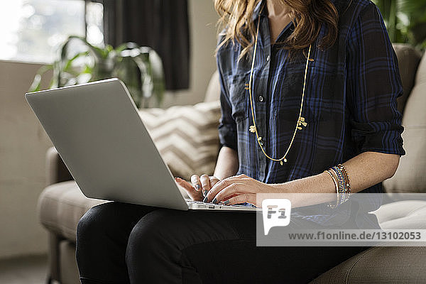 Mittelgruppe einer Frau  die einen Laptop benutzt  während sie auf einem Sofa sitzt