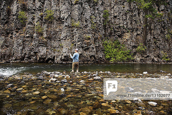 Rear view of man fly fishing at river against rock formations