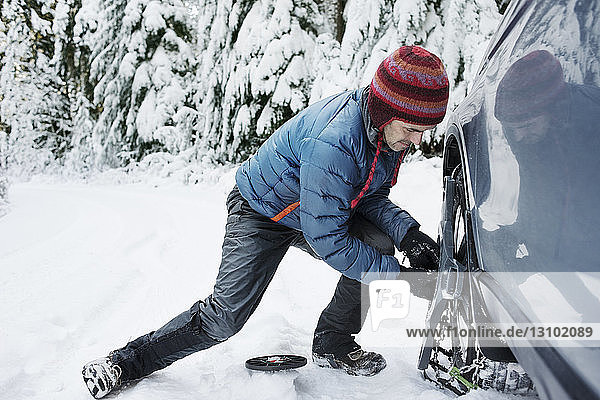 Man repairing car wheel on snow covered field