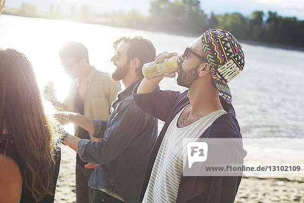 Man having drink while standing with friends against river