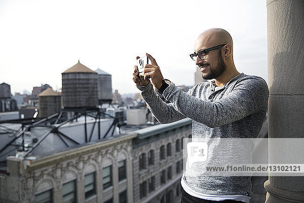 Lächelnder Mann fotografiert mit Smartphone auf dem Balkon