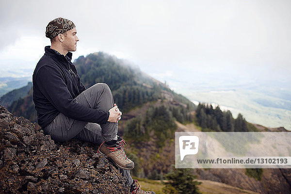 Nachdenklicher männlicher Wanderer sitzt auf Berg