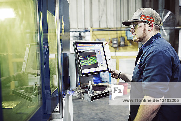 Seitenansicht eines Arbeiters  der einen Desktop-Computer bei der Arbeit in einer Stahlfabrik benutzt