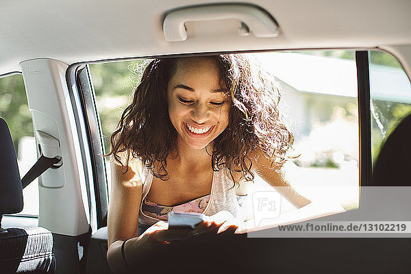 Lächelnde Frau benutzt Mobiltelefon  während sie sich ans Autofenster lehnt