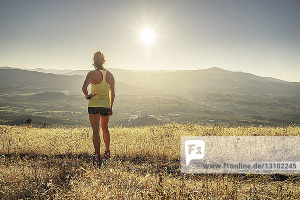 Rückansicht einer Frau  die mit der Hand in der Hüfte auf einem Berg vor klarem Himmel an einem sonnigen Tag steht