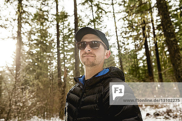 Low angle view of man wearing sunglasses hiking in forest during winter