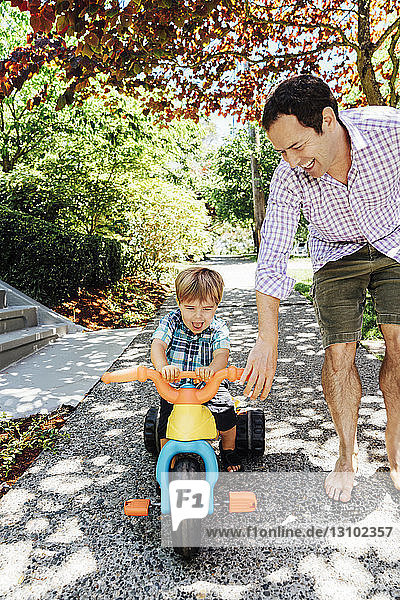 Happy father helping son ride tricycle in park
