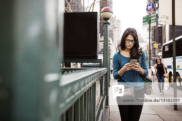 Junge Frau benutzt Smartphone beim Gehen auf dem Bürgersteig