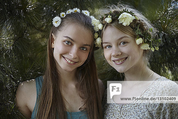 Porträt von glücklichen Freunden mit Diademen  die bei Pflanzen im Park stehen
