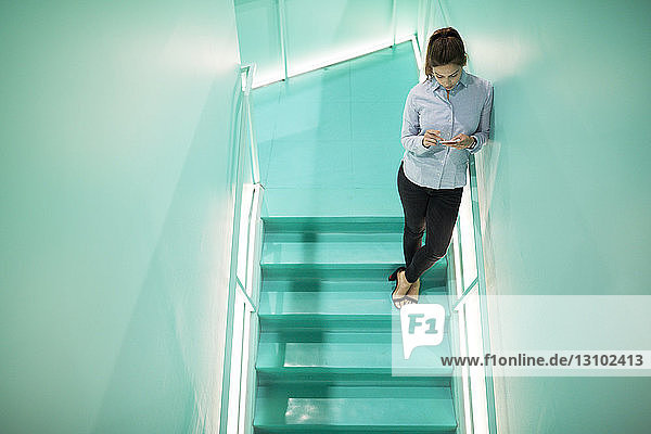 Schrägansicht einer Geschäftsfrau  die ein Smartphone benutzt  während sie auf einer Treppe steht