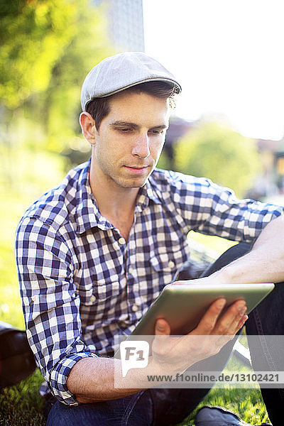 Mann benutzt digitales Tablett  während er auf einem Rasenplatz sitzt