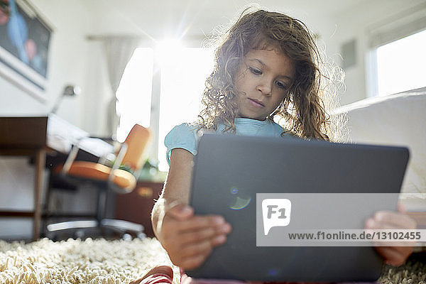 Low angle view of girl using tablet computer while kneeling on rug in bedroom