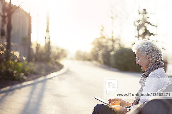 Ältere Frau mit Tablet-Computer auf Bank am Gehweg